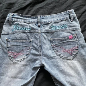 Jätte coola bootcut byxor - Säljer ett par ljusblå jeansbyxor med broderad detalj och text på bakfickan. Det är en lågmidjad bootcut model med yk2 stil. Det är storlek w27 vilket motsvarar S. Jag är 166 cm lång och benen är perfekt längd på mig. Inte använda alls mycket 2-3 gånger, mycket fint skick. Säljer då de inte kommer till användning. Väldigt unika och snygga.