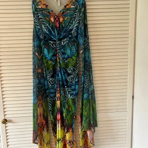 Dramatisk långklänning från Bodyflirt Boutique - Säljer en långklänning från Bodyflirt Boutique med tropiskt mönster i blått, grönt och inslag av orange. Klänningen har långärmade, slitsade, vida ärmar och v-ringning. Perfekt för dig som gillar färg och mönster!