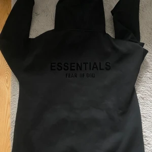 Svart Essentials Fear of God hoodie - Säljer en svart hoodie från Essentials Fear of God. Tröjan har huva, magficka och tryck både fram och bak. Perfekt för dig som gillar streetwear och vill ha en stilren look.