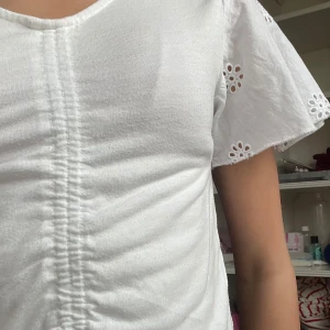 Tröja med blomvolang!  - Säljer en söt tröja med blomvolang som ärmar. Är ribbad med stretchtyg i mitten, som en snygg och cool detalj. Perfekt för en sommar middag med familjen! 