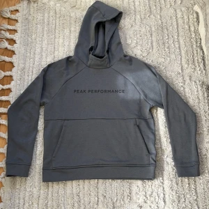 Grå hoodie från Peak Performance - Säljer en stilren grå hoodie från Peak Performance i storlek XS. Tröjan har huva, lång ärm och en stor magficka framtill. Perfekt för en avslappnad look och enkel att matcha med det mesta.