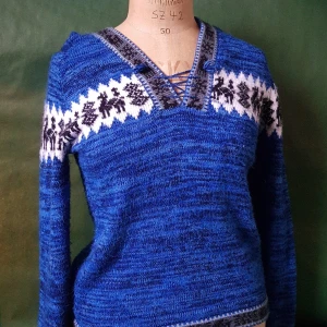 Blå stickad hoodie med mönster - Säljer en blå stickad hoodie med vit och svart mönsterdetalj över bröstet och axlarna. Tröjan har snörning vid v-ringningen och en mysig huva. Perfekt för kyliga dagar och har långa ärmar.