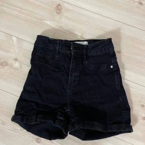 Svarta jeansshorts från Gina  - Svarta jeansshorts med hög midja och uppvikta benslut. Klassisk femficksmodell med dragkedja och knapp framtill. 