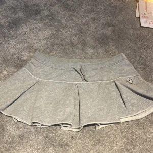 Grå kjol från Svea - Säljer en ljusgrå kjol från Svea i mjukt bomullsmaterial. Kjolen har volang nertill, bred resår i midjan och en liten broderad krona på sidan. Perfekt för en avslappnad men söt look