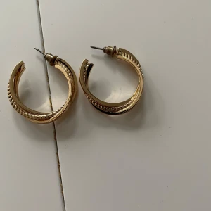 Guld färgade  örhängen i halvcirkel - Säljer ett par snygga guldiga örhängen i halvcirkel med räfflad detalj längs kanten. Perfekta för att lyfta din stil med en klassisk touch. Passar till många olika outfits!