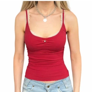 Röd ribbad linnetopp med spetsdetaljer - Snygg röd ribbad linnetopp med smala axelband och spetsdetaljer vid urringningen. Toppen har en liten rosett framtill och är figurnära i modellen. De två första bilderna är lånade av fd säljare!