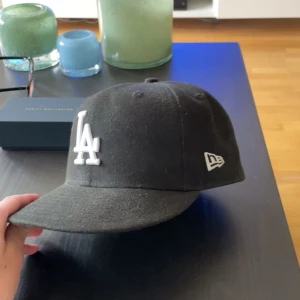 Svart LA keps från New Era 59FIFTY - Säljer en svart New Era 59FIFTY keps med LA-logga i vitt framtill. Klassisk modell med böjd skärm och broderade detaljer. Passar dig som gillar sportig stil och streetwear.