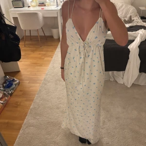 Vit långklänning med blått blommönster  - Säljer en vit långklänning från Adoore med små blå blommor. Endast använd en gång och är i bra skick