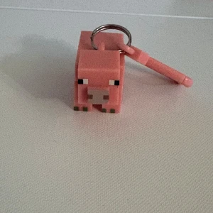 Minecraft gris nyckelring - Säljer en söt nyckelring i form av en gris från Minecraft. Nyckelringen är rosa och har en fyrkantig, pixlig design som påminner om spelet. Perfekt att hänga på väskan eller nycklarna för alla Minecraft-fans!
