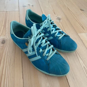 Blå Adidas Gazelle sleek sneakers - Säljer ett par blå Adidas Gazelle Sleek sneekers i den första kollektionen av smalare modeller. Skorna har klassisk retrodesign med Adidas-logga på hälen och sidan med  ljusblå ränder och snörning. Perfekta för dig som gillar sportig och stilren look.