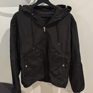 Moncler windbreaker - Säljer en svart windbreaker från Moncler i storlek L. Jackan har en Moncler logga på ärmen och ränder på luvan Perfekt för blåsiga vårdagar. Skriv vid funderingar.