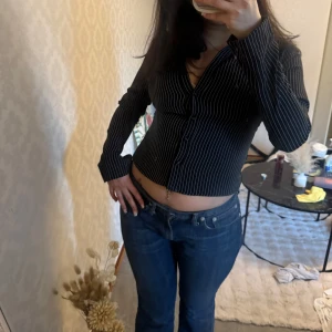 Svart skjorta med vita ränder - Svart skjorta med smala vita ränder. Skjortan har lång ärm, v-ringning och knäppning framtill. Snygg passform som sitter tight 🖤