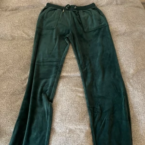 Mörkgröna mjukisbyxor från Juicy Couture - Säljer ett par mörkgröna mjukisbyxor från Juicy Couture med bred resår och snörning i midjan. Byxorna har stora fickor fram och bak, samt broderad logga på ena fickan. Tyvärr bara använda 1 gång. ( 2 av bilderna blev upp och ner 😅 )