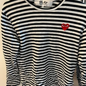 Randig långärmad tröja från Comme des Garçons Play - Säljer en randig långärmad tröja från Comme des Garçons Play med det ikoniska röda hjärtat broderat på bröstet. Perfekt för dig som gillar stilrena plagg med en twist. Storlek M men passar S