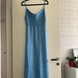 Ljusblå långklänning med smala axelband - Säljer en ljusblå långklänning i satin med smala axelband och lätt draperad urringning. Perfekt om man vill känna sig mer uppklädd eller lite finare! Säljer den vidare då jag valde att använda en annan klänning till ett bröllop. Jag är 165cm och den går ner till fotvristen.