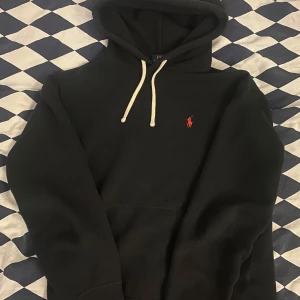 Ralph Lauren hoodie - Säljer en svart hoodie från Ralph Lauren. Tröjan har vita snören, huva  och en stor magficka framtill. Perfekt för en avslappnad och stilren look. Tröjan är i mycket bra skick!