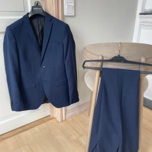 Jack&Jones kostym - Säljer en stilren mörkblå kostym från Jack & Jones. Använd tre gånger så den är i väldigt bra skick.                                                                                   Storlek: 44 och S på skjortan.                                         Passform: Super slim fit.                                                        Hör av er vid frågor!