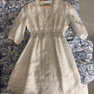 Vit klänning med spetsdetaljer - Superfin vit klänning med v-ringning och spetsdetaljer längs ärmar, midja och nederkant. Klänningen har trekvartsärm och är perfekt för sommaren! Har endast använts en gång och har inga anmärkningar.