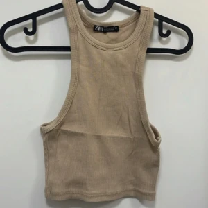 Beige ribbad linnetopp från Zara - Säljer en beige ribbad linnetopp från Zara. Toppen är ärmlös med rund halsringning och croppad passform. Perfekt för varma dagar eller som lager under en skjorta.