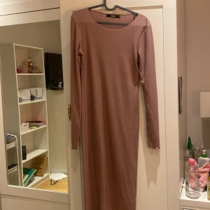Rosa långärmad ribbad klänning från BikBok - Säljer en enkel och stilren långärmad klänning från BikBok i en mjuk, ljusrosa ribbad kvalitet. Klänningen är kroppsnära och har rund halsringning samt hellångt snitt. Perfekt för dig som gillar minimalistisk stil.