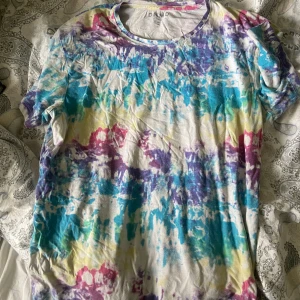 Färgglad tshirt  - Säljer en färgglad t-shirt från DNMD i storlek M. T-shirten har ett unikt abstrakt mönster i blått, lila, gult och rosa på vit botten. Klassisk rund halsringning och korta ärmar. Perfekt för dig som gillar färg och vill sticka ut!