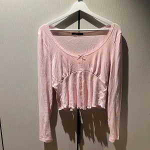 Ljusrosa croppad topp från Gina Tricot - Söt ljusrosa croppad topp från Gina Tricot med lång ärm, spetsdetaljer längs urringningen och en liten rosett framtill. 
