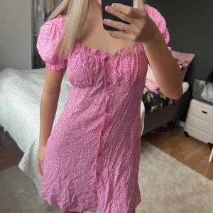 Rosa blommig sommarklänning  - Supersöt rosa klänning med små vita blommor, puffiga kortärmar och knappar framtill🩷 