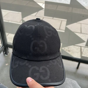 Svart keps från Gucci med GG-mönster - Snygg svart keps från Gucci med diskret GG-mönster över hela kepsen. Kepsen har böjd skärm och justerbart spänne baktill i skinn. Tillverkad i bomullsmaterial med exklusiv känsla.