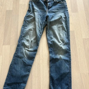 Lee Marion Straight jeans W27 L31 - Säljer ett par klassiska blå Lee Marion Straight jeans med raka ben och normal passform. Byxorna har fem fickor, dragkedja och knapp framtill samt slitning på vänster lår för en cool look. Midjemått ca 35 cm se sista bild 