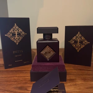 Initio Side Effect Eau de Parfum - Lyxig parfym från Initio i modellen Side Effect. Flaskan är mörklila med gulddetaljer och har en fyrkantig form med dekorativt mönster i guld. Kommer i elegant ask med matchande design. Rymmer 90 ml Eau de Parfum.