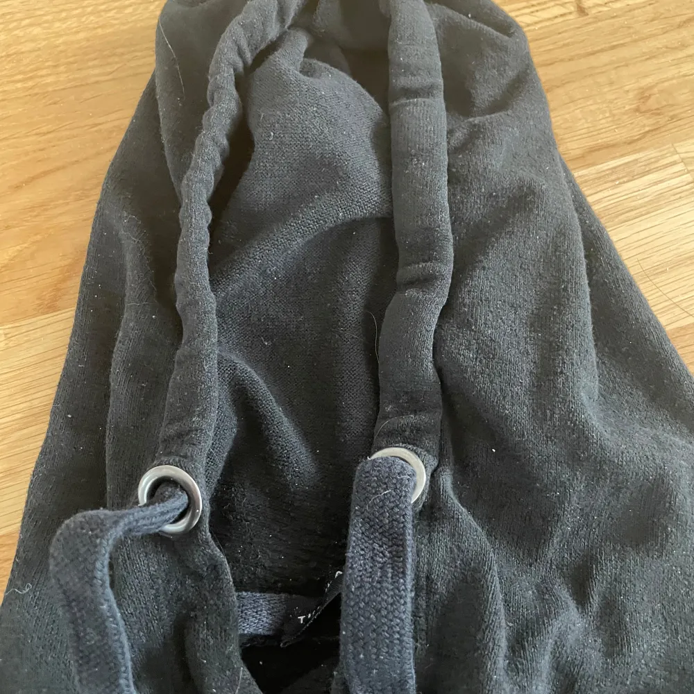 En svart hoodie från Label Collection med justerbar huva och dragsko. Tröjan har långa ärmar och är tillverkad i ett mjukt material som känns skönt mot huden. Perfekt för en avslappnad stil.. Neuletakit & Villapaidat.