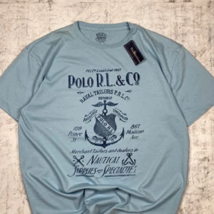 Ljusblå t-shirt från Polo RL & Co - Snygg ljusblå t-shirt från Polo RL & Co med marinblått tryck framtill. T-shirten har rund halsringning och korta ärmar. Perfekt för en avslappnad stil med nautiskt tema.