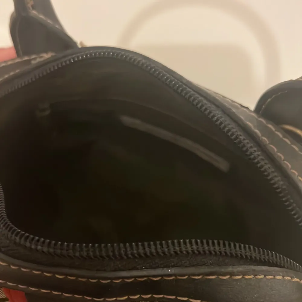 Säljer en snygg handväska från Tommy Hilfiger med svart och beige mönster, svarta handtag och detaljer i rött och grönt med guldfärgade knappar. Väskan har dragkedja och är perfekt för dig som vill ha en stilren accessoar.. Laukut & Käsilaukut.