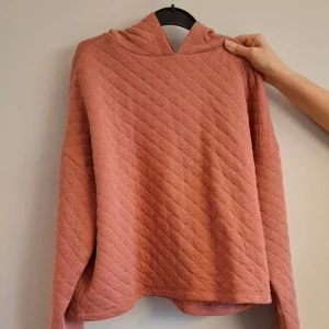 Rosa quiltad hoodie - Säljer en hoodie i damstorlek S. Tröjan är i en dämpad rosa färg med luva och långa ärmar. Den är knappast använd och har en nyskick.