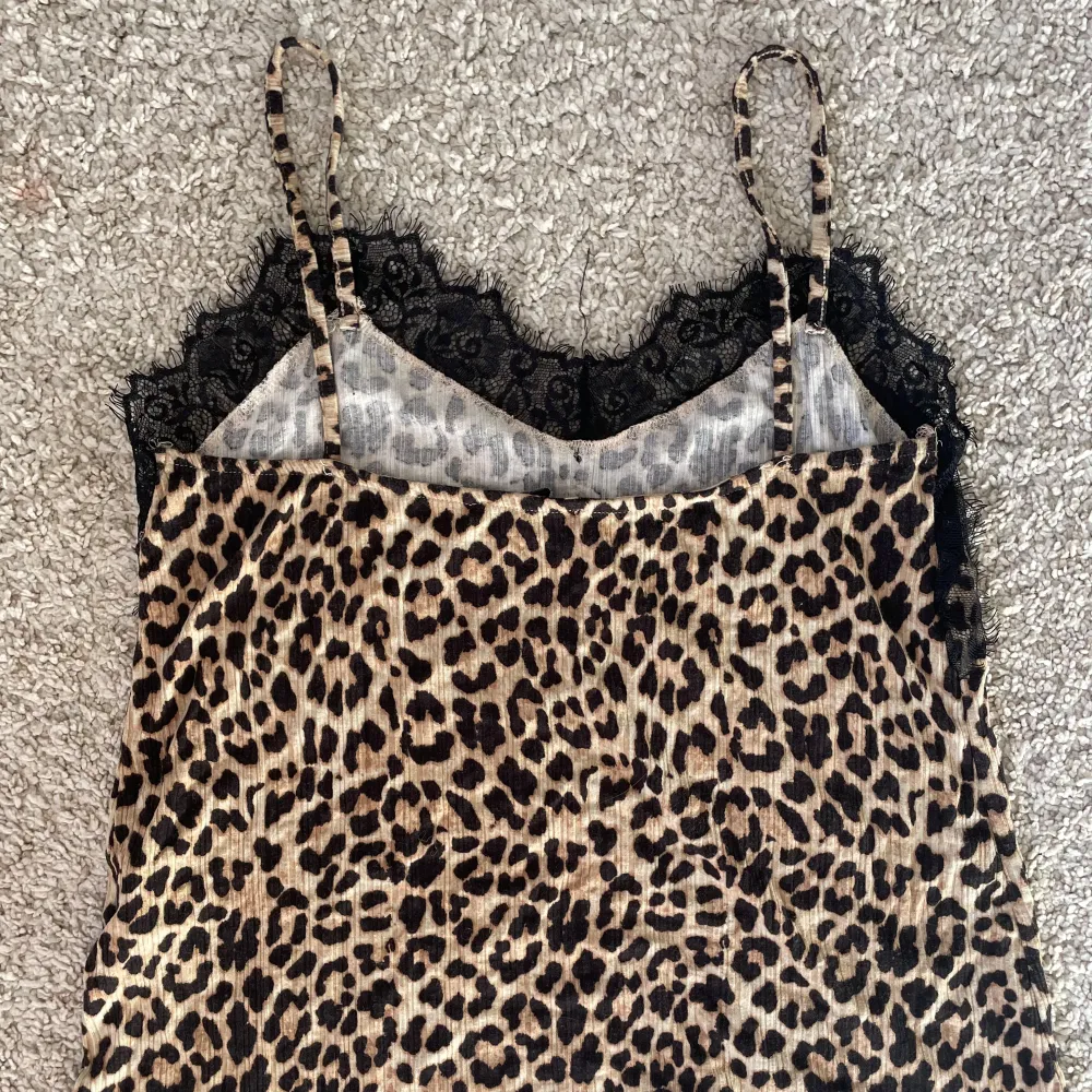 Säljer ett leopardmönstrat linne med tunna axelband och svart spets upptill. Toppen har en croppad passform och är perfekt för dig som vill sticka ut med ett djurmönster. Materialet känns mjukt och följsamt.. Yläosat.