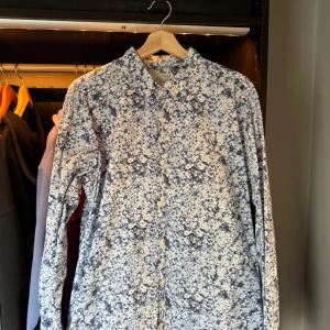 Mönstrad skjorta från Knowledge Cotton Apparel - Snygg skjorta med vitt och blått mönster (blommig?) från Knowledge Cotton Apparel. Slimfit. Tunnare tyg som passar perfekt till sommaren.  Tillverkad i 100% ekologisk bomull för en skön känsla och stilren look.