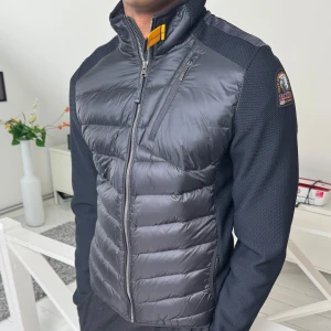 Svart pufferjacka/hybridjacka från Parajumpers - Säljer en svart pufferjacka från Parajumpers med quiltad framsida och rygg, samt släta ärmar. Jackan har dragkedja, hög krage med gul detalj och en bröstfickan med dragkedja. Märkespatch på ena ärmen. Storleken är Youth L som är XS/S i mans storlek 