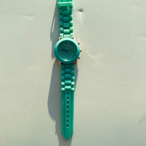 Turkos klocka i nyskick - Klockren (ha!) grön klocka / armbandsur med gummiband och urtavla med detaljer i guld. Oanvänd, men behöver bytas batteri då den legat i smyckesskrinet ett tag.   Hämtas i Stockholm eller skickas mot porto.  Kolla gärna mina andra annonser också, stor utrensning pågår. Samfraktar gärna!