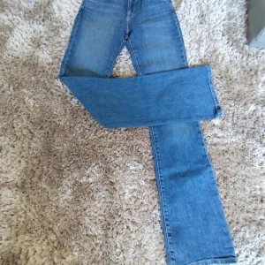 Blå bootcut jeans från Wrangler - Säljer ett par klassiska blå jeans från Wrangler med bootcut passform. Jeansen har hög midja, snygga bakfickor med ikonisk W-söm och läderpatch med logga. Tillverkade i slitstarkt denim och perfekta för dig som gillar en tidlös look.