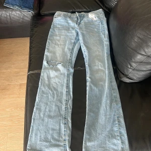 Ljusblå bootcut jeans med slitning - Snygga ljusblå jeans med bootcut passform och hål på ena knät. Klassisk femficksmodell med knappar på bakfickorna. Perfekta för en avslappnad och trendig look.
