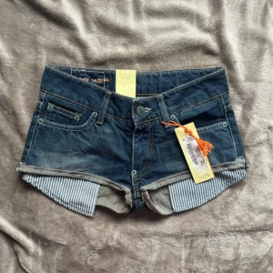 Blå jeansshorts med randiga detaljer - Snygga blå jeansshorts med klassisk femficksdesign och uppvikta ben med blåvit randigt tyg på insidan. Shortsen har låg midja, coola kontrastsömmar och detaljerade bakfickor. Perfekta för varma dagar och en avslappnad look. Prislappen är kvar🫶🫶❤️❤️