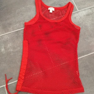 Röd nätlinne från Melrose - Säljer ett rött linne från Melrose i mesh/nätmaterial. Linnet är ärmlöst och har en cool snörningsdetalj på sidan. Perfekt för lager-på-lager eller som statement-piece till sommaren.