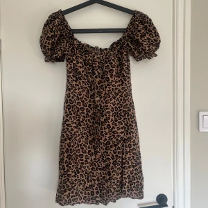 Leopardmönstrad kort klänning - Superfin kort klänning med leopardmönster och puffiga korta ärmar. Klänningen har knappar framtill och en smockad, elastisk urringning som kan bäras offshoulder. Perfekt för dig som vill sticka ut med en trendig look.