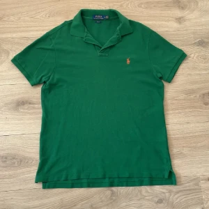 Grön pikétröja från Polo Ralph Lauren - Snygg grön pikétröja från Polo Ralph Lauren i slim fit-modell. Klassisk krage, korta ärmar och den ikoniska broderade loggan på bröstet. Tillverkad i mjuk bomull som känns skön mot huden. Perfekt för en clean och sportig look.