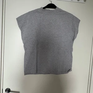 Grå ärmlös topp från Zara - Säljer en enkel och stilren grå ärmlös topp från Zara. Toppen har en rak passform, högre halsringning och är gjord i mjuk bomull. Perfekt att styla med jeans eller kjol för en clean look.