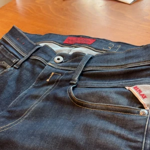  Replay jeans - Säljer ett par mörkblå jeans från Replay, modell Rocco . Klassisk femficksdesign med kontrastsömmar, Replay-logga på fickan och läderpatch bak. Snygg passform