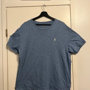 Blå t-shirt från Polo Ralph Lauren - Snygg blå t-shirt från Polo Ralph Lauren med klassisk broderad logga på bröstet. T-shirten är i mjuk bomull och har en normal passform med korta ärmar. Perfekt basic-plagg med stilren look och rund halsringning.