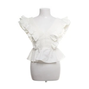 Vit blus med volanger och v-ringning - Supersöt vit blus med djup v-ringning både fram och bak, stora volanger längs axlarna och en peplumkant. Toppen har dragkedja i ryggen och är ärmlös. Perfekt för dig som vill sticka ut med en romantisk och trendig look.