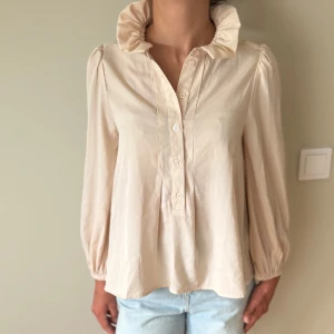 Blus - Beige blus med volang i kragen. 