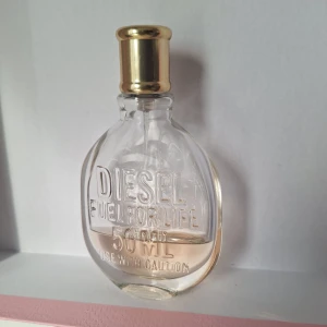 Diesel Fuel For Life 50ml parfym - Diesel Fuel For Life parfym i en genomskinlig oval glasflaska med ingraverad text och guldfärgad spraykork. Flaskan rymmer 50 ml och innehållet är ljusrosa. Snygg och stilren design som sticker ut i badrumshyllan.